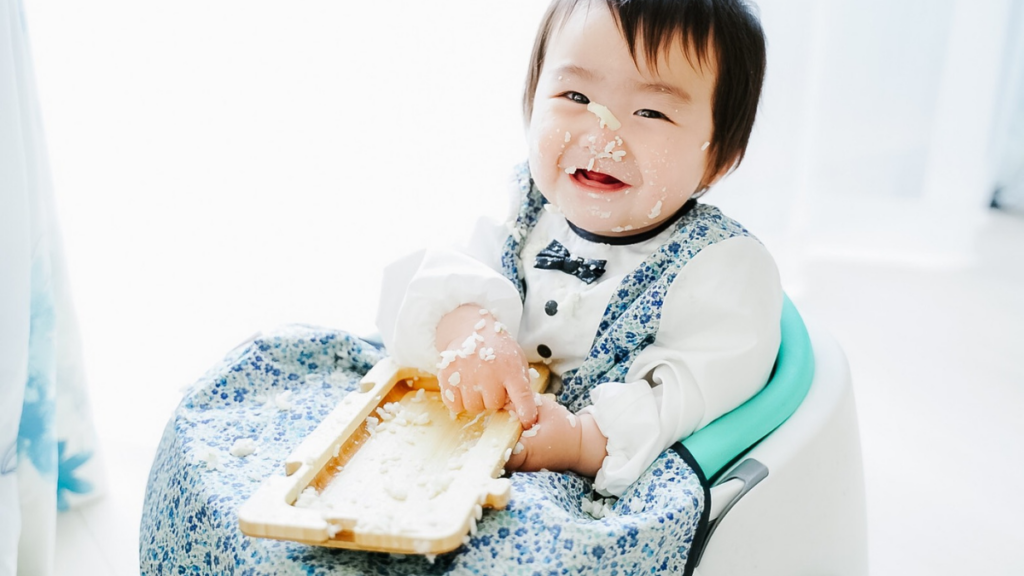 手づかみ食べで顔やエプロンに食べこぼしが付いている赤ちゃん